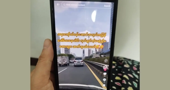 Hand holding a phone showing a TikTok video advertising factory job recruitment with high pay for young workers, illustrating the online job scams targeting unemployed garment workers