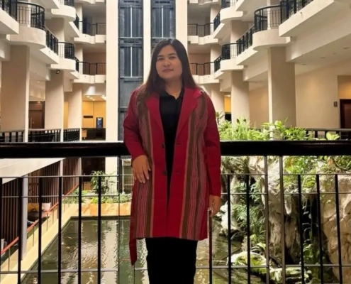 Mu Angela, newly elected chairperson of the Karenni State Consultative Council (KSCC), standing in a traditional red Karenni jacket at a building atrium