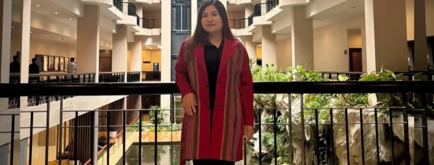 Mu Angela, newly elected chairperson of the Karenni State Consultative Council (KSCC), standing in a traditional red Karenni jacket at a building atrium